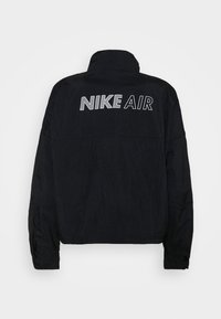 Veste Nike Air noire avec un col élevé, des manches longues et un grand logo en texte blanc dans le dos. Tissu texturé avec une coupe décontractée.