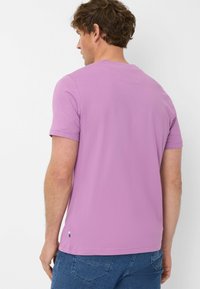 T-shirt in cotone viola a maniche corte con collo rotondo, dotato di orlo cucito e di un piccolo tag colorato in basso a sinistra.