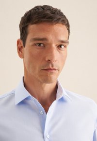 Camicia azzurro chiaro con colletto strutturato, caratterizzata da un motivo decorativo all'interno del colletto. Tessuto liscio e vestibilità su misura.