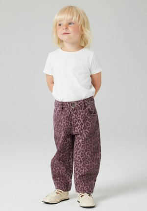 Pantalons en denim imprimés léopard dans des teintes de violet, associés à une chemise blanche à manches courtes unie et des chaussures de couleur claire.