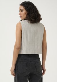 Haut sans manches gris rayé avec un design court, associé à un jean noir taille haute. Des textures simples et des lignes subtiles mettent en valeur l'ensemble.
