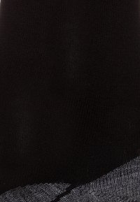 Schwarze Socke mit strukturierter Oberfläche und einem kontrastierenden grauen Bund. Das Material wirkt dehnbar und körperbetont.