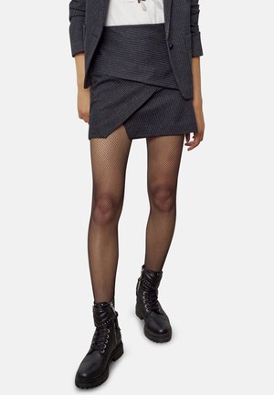 Jupe mini à rayures noires avec un design asymétrique, associée à des collants en résille et des bottes de combat noires avec des accents métalliques.