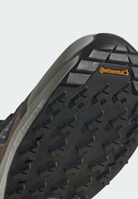Semelle de chaussure avec un motif de bande de roulement profond et le logo Continental en orange sur caoutchouc noir, conçue pour une meilleure adhérence et durabilité.