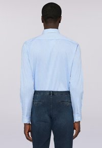 Světle modrá pruhovaná košile s dlouhými rukávy, úzkým límcem a zadním sedlem, kombinovaná s tmavými džíny.