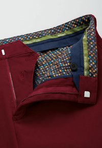 Bordeauxrode broek met een gestructureerde voering aan de binnenkant met een geometrisch patroon in meerdere kleuren, waaronder blauwe, oranje en groene accenten.