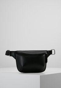 Riñonera de imitación cuero negra con forma curva, bolsillo frontal con cremallera, correa ajustable y detalles en metal plateado. Textura suave.