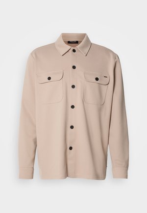 Beige langærmet skjorte med knapper og krave, to brystlommer med klapper og sorte knapper ned foran.