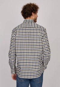 Chemise à carreaux dans des tons de bleu marine, crème et olive. Elle possède des manches longues, un col classique et des fermetures à boutons avec un ourlet arrière droit.