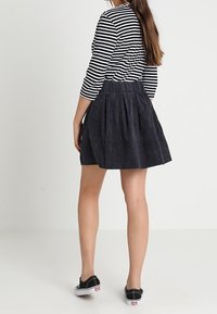 Falda de mezclilla oscura con diseño plisado, acompañada de una camiseta de manga larga a rayas en blanco y negro. La modelo lleva zapatos negros tipo mocasín.