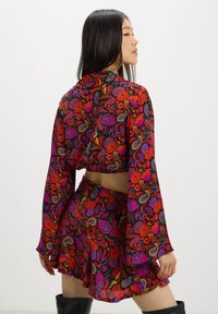Set a due pezzi con motivo floreale rosso, composto da un top cropped con maniche lunghe e una gonna svasata, realizzato in tessuto leggero.