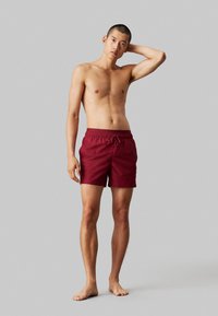 Bañador burdeos hecho de material ligero, con una cintura elástica y cordón ajustable, de longitud por encima de la rodilla y una textura suave.