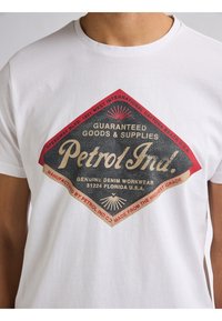 Bílý bavlněný tričko s vintage grafickým logem ve tvaru diamantu v červené a černé barvě se vzorem "Petrol Ind." a detaily slunečního paprsku.