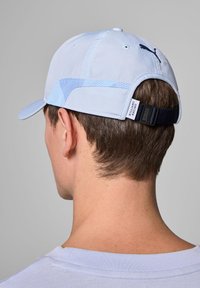 Jasnoniebieska czapka z materiału z teksturowaną boczną panelem, zakrzywionym daszkiem i regulowanym czarnym paskiem z białym napisem.