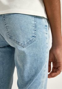 Lyseblå denimjeans med en konisk pasform, der har en baglomme med en synlig syning og en glat, tekstureret overflade.