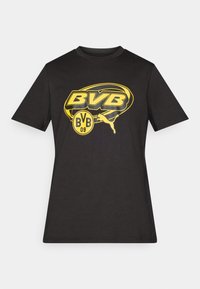Sort kortærmet T-shirt med gult BVB-logo, rundt emblem og Puma-kat grafik centreret på brystet.