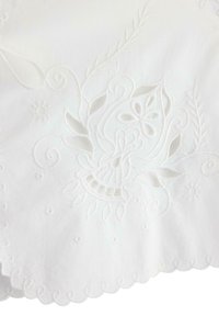 Tessuto bianco con ricami intricati che presentano disegni floreali e fogliari. I dettagli ritagliati e i bordi ondulati aggiungono texture e interesse visivo.