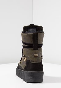 Bottine avec une tige en khaki texturé et des accents en daim noir. Présente une semelle épaisse, des matériaux métalliques et un col rembourré.