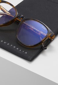 Gafas de sol con patrón de carey y lentes espejados azules descansando sobre un estuche negro texturizado, con letras blancas que dicen "AUSTRALIA".