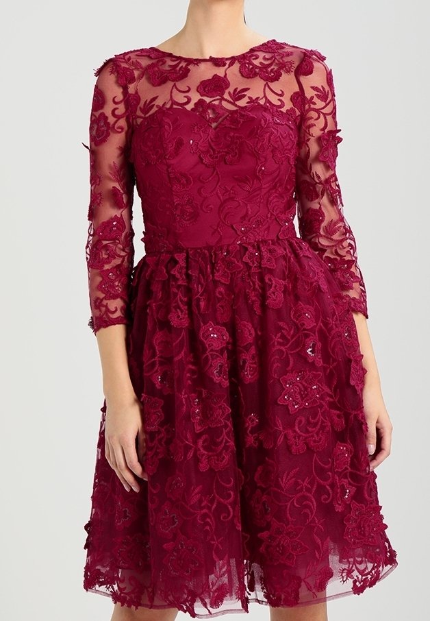 Robe bordeaux longueur genou avec superposition en dentelle florale, manches trois-quarts transparentes, corsage ajusté et jupe légèrement évasée.