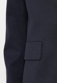 Giacca suit tailor in blu navy caratterizzata da un design elegante, texture liscia e una singola tasca sul petto. Stile minimalista senza pattern visibili.