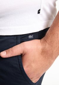 Witte t-shirt met korte mouwen, gecombineerd met marineblauwe broek met een zijzak en een klein "Petrol Industries" label op de tailleband.