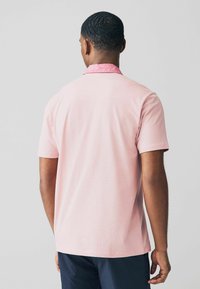 Vaaleanpunaisesta kankaasta valmistettu lyhythihainen polo-paita, jossa on kuviollinen vaaleanpunainen kaulus. Sileä rakenne rentoa istuvuutta ja sivuhalkioita varten.