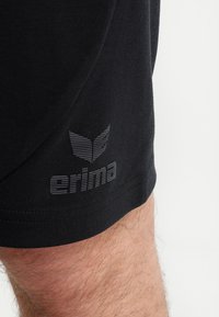 Shorts de sport noirs en tissu doux, ornés d'un logo gris foncé au bas. Le design est simple avec une coupe régulière.