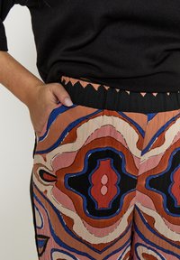 Losvallende broek met een kleurrijk abstract patroon in roest, roze, blauw en zwart, voorzien van een geplooide tailleband en zijzakken.