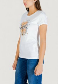 Camiseta de algodón blanca con mangas cortas, con un diseño gráfico floral en naranja y azul, y el texto "LIU JO" destacado.