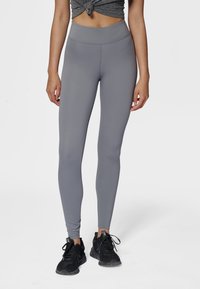 Grå leggings i stretchigt material med slät yta, hög midja och utan synliga mönster eller detaljer. Bärs med svarta sneakers.