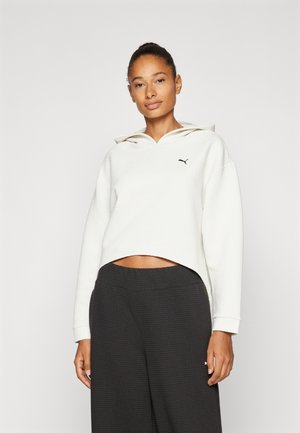 Sudadera blanca con textura y capucha, de corte cropped y con un pequeño logotipo negro. Combinada con pantalones oscuros de textura suelta.