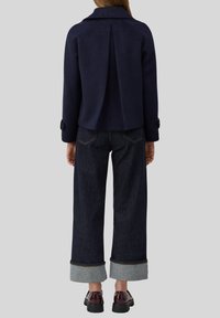 Marineblauer Wollmischjacke mit FaltenDETAIL auf der Rückseite, kombiniert mit dunkelblauen Jeans mit umgeschlagenem Saum und burgunderfarbenen Schuhen.