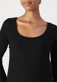 Schwarz geripptes Langarmoberteil mit weitem Rundhalsausschnitt, glatter Textur und figurbetonendem Schnitt, geeignet zum Schichten oder als eigenständiges Kleidungsstück.