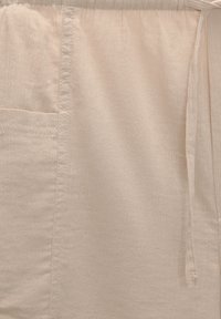 Short beige en tissu léger, avec une ceinture élastique et un détail noué, une texture subtile et une poche latérale.