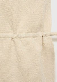 Beige knitted fabric with a soft texture, featuring a gathered seam detail and a subtle sheen. No distinct patterns or embellishments present.