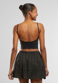 Zwart cropped top met dunne bandjes, gecombineerd met een zwarte textuurlaagrok. De stof lijkt zacht en vloeiend, met een losse pasvorm.