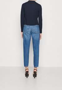 Granatowa bluzka z długim rękawem o skróconym kroju, zestawiona z jasnoniebieskimi spodniami typu straight leg z klasycznymi kieszeniami naszytymi i podwiniętymi nogawkami. Czarne sandały na obcasie.