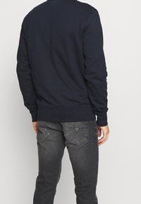 Granatowa bluza z długimi rękawami i ściągaczami na mankietach, zestawiona z szarymi, zwężanymi dżinsami z trójkątnym logo na tylnych kieszeniach.