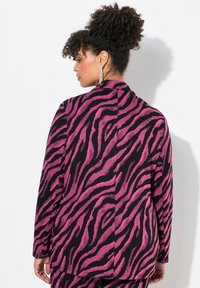 Blazer con stampa zebra caratterizzato da una combinazione di colori nero e rosa acceso, maniche lunghe e una vestibilità sartoriale con colletto a revers e spacco singolo.
