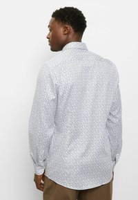 Langärmliges Hemd aus weißem Stoff mit kleinen blauen und gelben Punkten, mit Standardkragen und abgerundetem Saum.