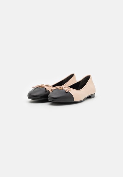 Ballerines en cuir nude avec un empiècement noir à l'avant. Présentent un petit nœud décoratif à l'avant et une semelle en caoutchouc noir, de faible hauteur.