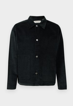 Veste en velours côtelé noir avec un col, des poches avant et des boutons argentés. Présente des côtes verticales dans la texture du tissu. Design simple.