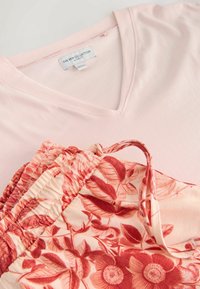 Top de culoare roz deschis cu decolteu în V, asortat cu pantaloni scurți crem cu un model floral roșu și detalii cu talie strânsă.