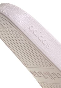 Bílá podešev tenisky z gumy s texturovaným vzorem proti skluzu a raženým logem. Hladký horní okraj s jemným leskem.