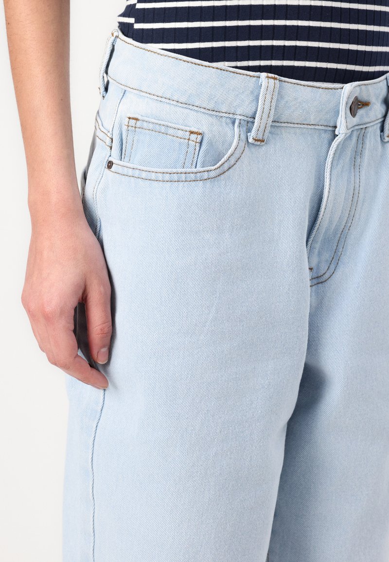 Jeans en denim bleu clair à taille haute, avec des coutures visibles, des poches latérales et une coupe décontractée. La texture du tissu est subtilement tissée.