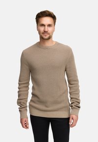 Beige gestrickter Pullover mit strukturiertem Muster, Rundhalsausschnitt und langen Ärmeln, kombiniert mit schwarzen Hosen.