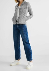 Šedá džínová bunda na zapínání na knoflíky, se dvěma předními kapsami a volným střihem, kombinovaná s modrými džínami s rovným střihem a bílými teniskami.