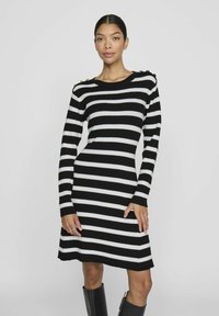 Robe tricotée à rayures noir et blanc avec des manches longues, un col rond et des accents de boutons dorés sur l'épaule. Silhouette ajustée avec un ourlet évasé.