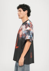 Sort oversized t-skjorte med et fargerikt abstrakt design i rødt, blått og hvitt, med ribbet rund hals og korte ermer.